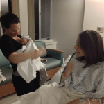 Mother holding child. Surrogate in the hospital bed looks on.
