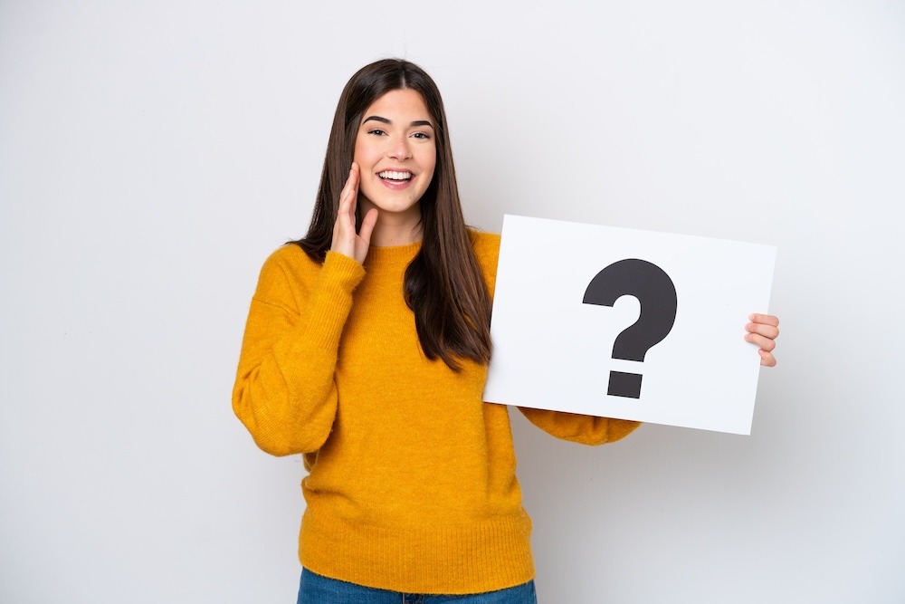 Young woman isolated on white background holding a placard with question mark symbol and shouting