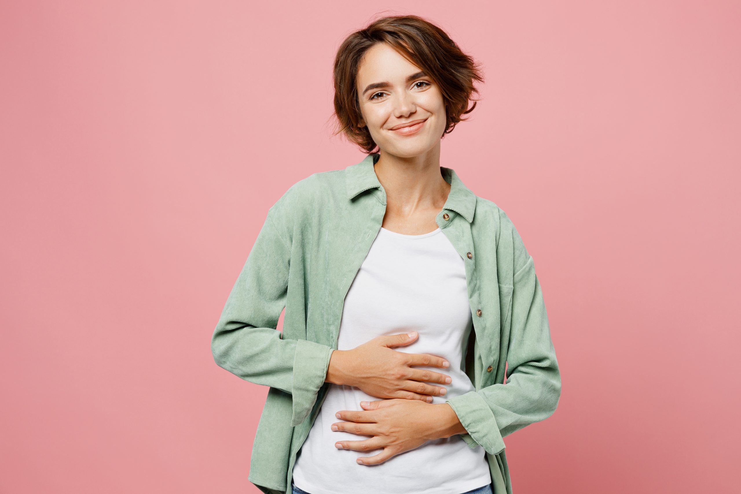 A woman standing in front of a pink background holding her belly